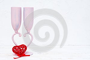 Two wine glasses form a heart-shaped legs and a red figured heart on a white table