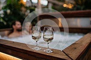 Two wine glasses on hot tub, couple relaxing, enjoying romantic wellness weekend in spa. Concept of Valentine's Day.