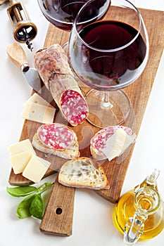 Two wineglass with red wine and assortment of cheese and salami.