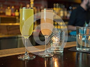 Two wineglasses filled with mimosa drinks sitting on a bar count