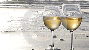 Two wineglasses on ocean beach. Glasses with white wine for romantic date, sea water. Sunset waves.