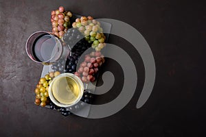 Two wineglasses with red and white wine, bottles and grapes on dark wooden background.