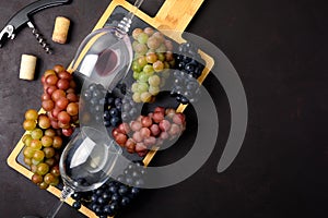 Two wineglasses with red and white wine, grapes, corkscrew and corks lying on dark wooden background