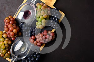 Two wineglasses with red and white wine, grapes, corkscrew and corks lying on dark wooden background