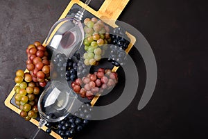 Two wineglasses with red and white wine, grapes, corkscrew and corks lying on dark wooden background.