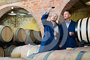 two winemakers with sample of wine in cellar.