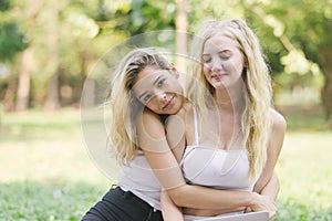 Two woman blonde hair friends embrace sitting in green park, Female friends hug together.