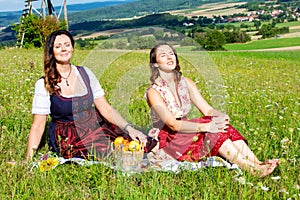 Two woman in dirndl sitting on blanket in meadow and enjoying the sun