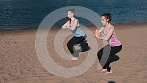 Two woman doing yoga on the beach by the river in the city. Beautiful view. Utkatasana pose.