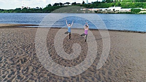 Two woman doing yoga on the beach by the river in the city. Beautiful view. Vrikshasana pose.