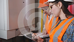 Two woman engineers checking technical data of heating system equipment in a boiler room