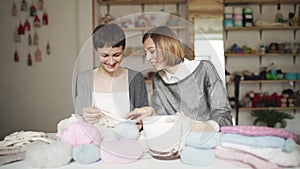 Two woman friends study knitting yarn wool sitting on table in home room