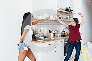 Two woman image that they are fighting on swords by wooden spatulas in kitchen