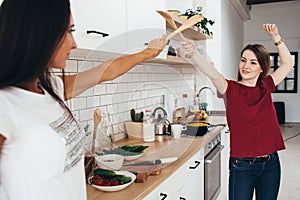 Two woman image that they are fighting on swords by wooden spatulas in kitchen