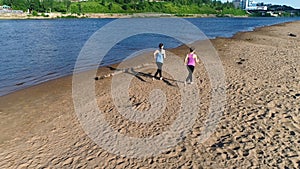 Two woman jogging along the sandy beach of the river at sunset. Beautiful city view.