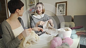 Two woman knitter talking and smiling in sewing studio. Woman knitting wool