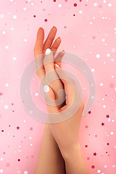 Two woman`s hands, white manicure on pink. Trendy nail gel polish. Holiday star confetti. Beauty salon flat lay.