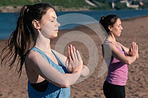 Two woman stretching yoga standing on the beach by the river in the city. Beautiful city view. Namaste pose.