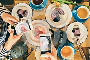 Two woman taking mobile photos of table fuul of desserts and tea. Top view. Food bloggers.