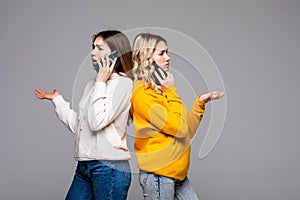 Two woman talk phones back to back isolated over gray background