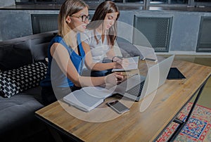 Two woman working together in office with laptop computer, writing a notary.