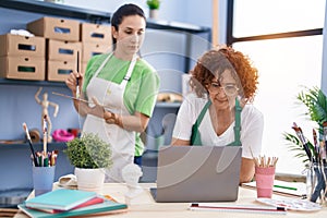 Two women artists drawing on notebook using laptop at art studio