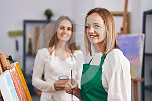 Two women artists smiling confident drinking coffee drawing at art studio