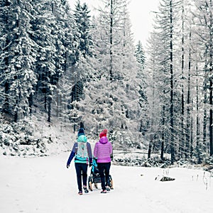 Two women with baby stroller enjoying motherhood in winter forest