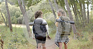 Two women with backpacks hike along a forest trail