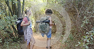 Two women with backpacks hike on a forest trail