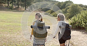 Two women with backpacks hike in a grassy outdoor setting