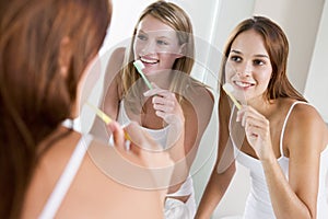 Two women in bathroom brushing teeth