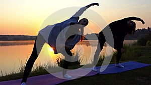 Two Women Bend Right And Left, While Raising Their Hands at Sunset in Slo-Mo