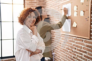 Two women business workers writing on cork board at office