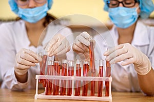 Two women in chemistry laboratory examining test tubes with red substance