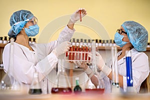 Two women in chemistry laboratory examining test tubes with red substance