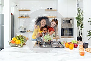 Two women a child, cooking together in a well-lit, homey kitchen, standing before a modern stove, embodying unity, love and