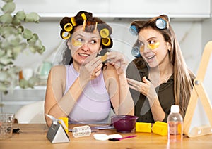 Two women curl their hair with curlers and use patches