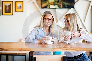 Two women of different generations drink coffee in a cafe and gossip. Girlfriends sit at table chatting and have a