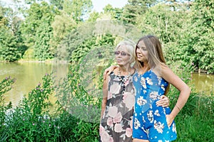 Two women of different generations are near a pond in the summer. Mother and daughter hugging. Grandmother and granddaughter.