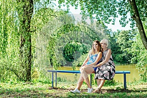 Two women of different generations sitting on a bench near a pond in the summer