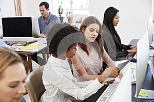 Two women discuss document at a desk in an open plan office