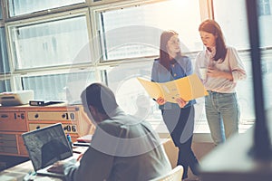 Two women discussing marketing plan in office. Man working on laptop. Coworking and open space office