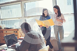 Two women discussing working plan in office. Man working on laptop. Coworking and open space office