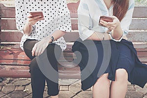 Two women in disinterest moment with smart phones in the outdoor, concept of relationship apathy and using new technology.