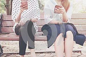 Two women in disinterest moment with smart phones in the outdoor, concept of relationship apathy and using new technology and smar