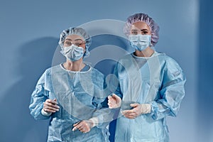 Two women doctors surgeons standing and looking at the camera on blue bakcground