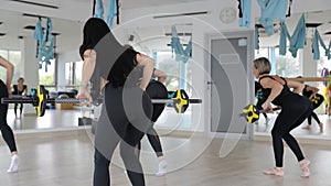 Two women are doing exercises with barbells in a gym