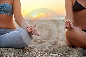 Two women doing group meditation on the beach on sunrise. Female friends doing yoga padmasana or lotus asana sitting on