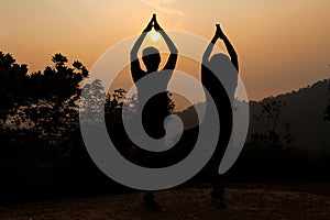 Two women doing yoga tree pose in silhouette during sunrise